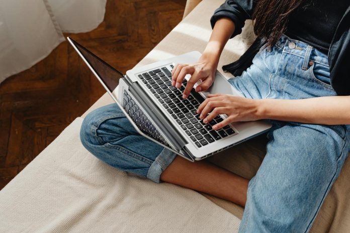 Close-up of a woman typing on a laptop, sitting cross-legged indoors.